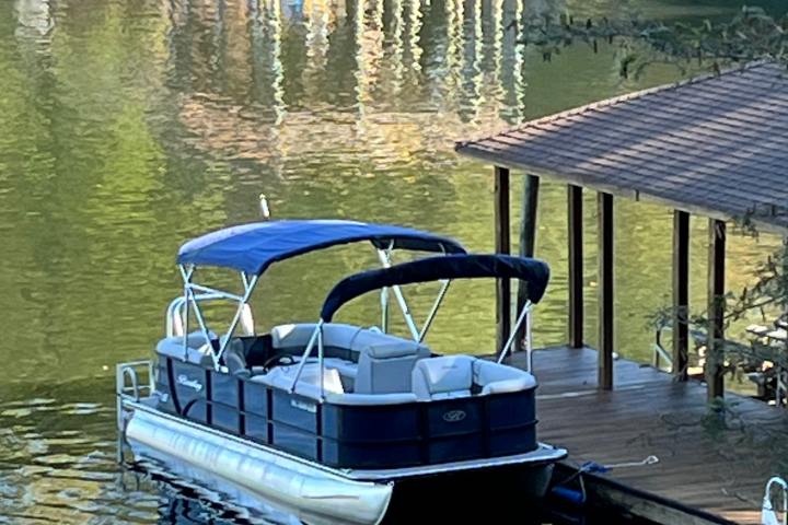 Pontoon boat docked at a wooden pier on a calm lake.