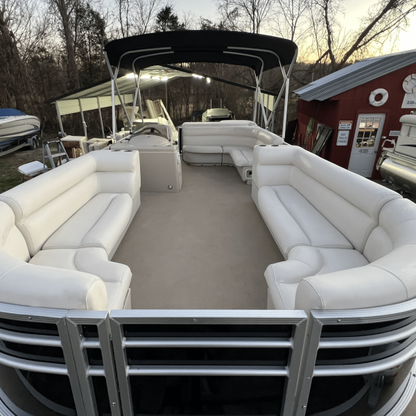 Interior of a pontoon boat with white seating under a canopy, parked near other boats and a red building.