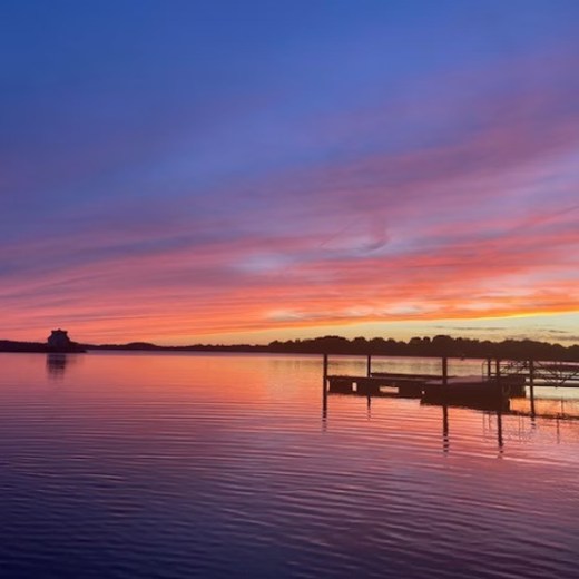 Serene lake at sunset with vibrant orange and purple sky, and a silhouetted pier.