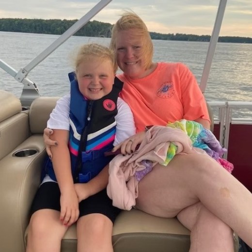 Two people smiling on a boat; one wearing a life jacket, the other holding a towel.