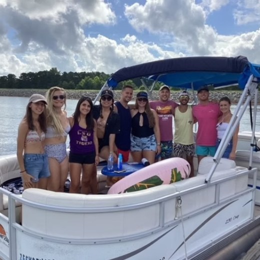 Group of people on a boat smiling at the camera under a cloudy sky.