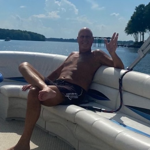 Man relaxing on a boat with a lake and trees in the background on a sunny day.