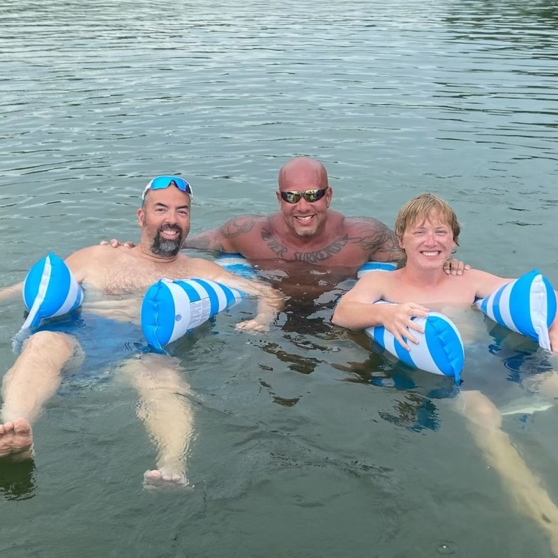 Three people in water with inflatable floats, smiling and relaxing.