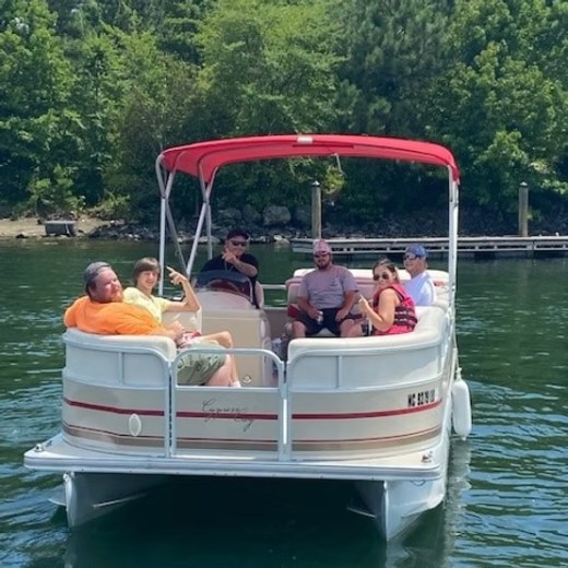 Group of six people relaxing on a pontoon boat with a red canopy on a sunny day.