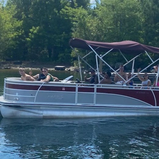 Group of people on a pontoon boat waving on a sunny day.