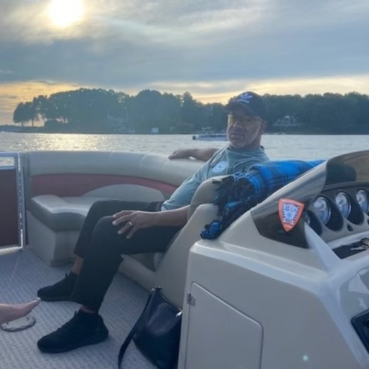 Person relaxing on a boat at sunset, with trees and water in the background.