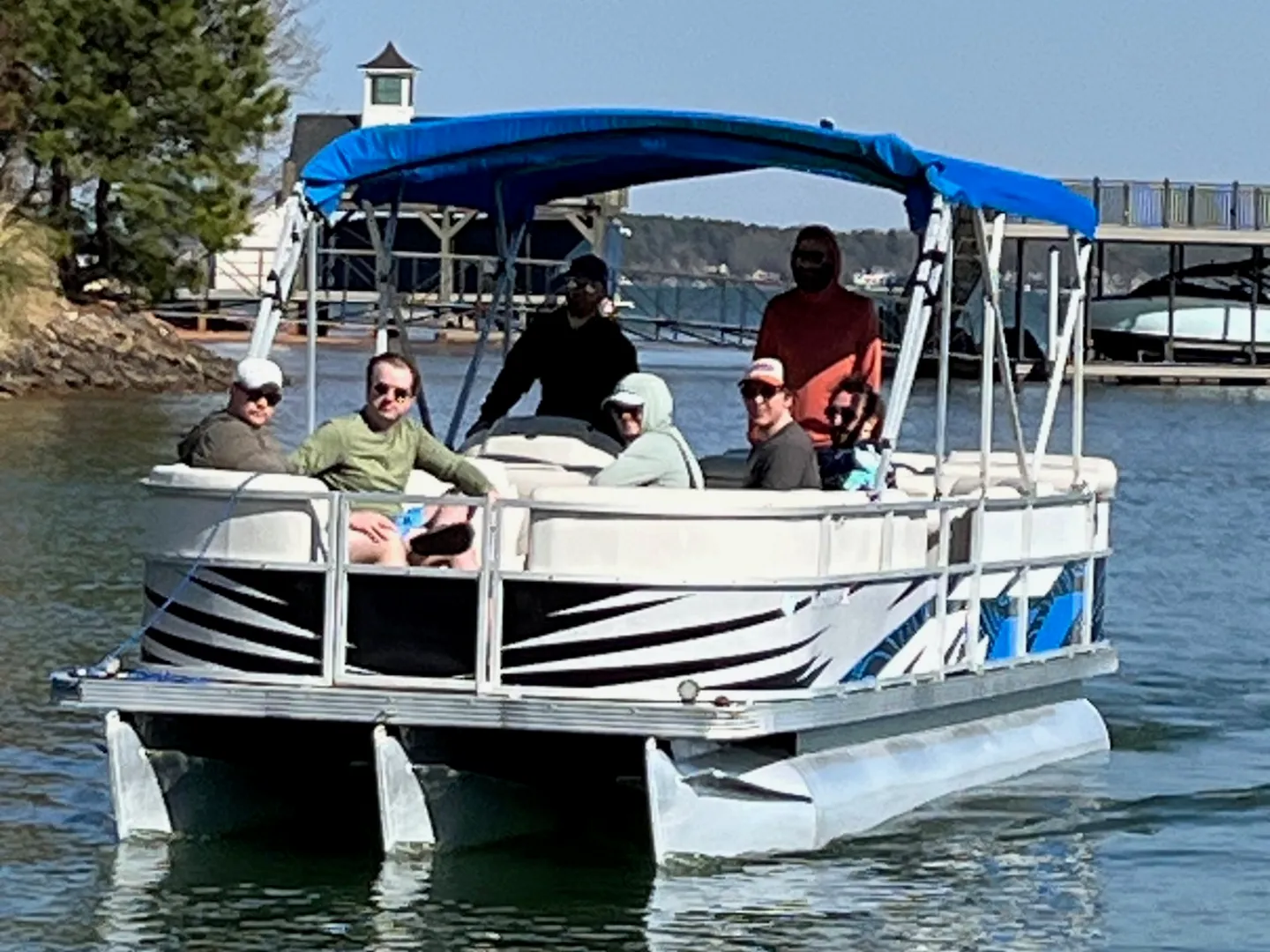 A group of people on a pontoon boat with a blue canopy on a sunny waterway.