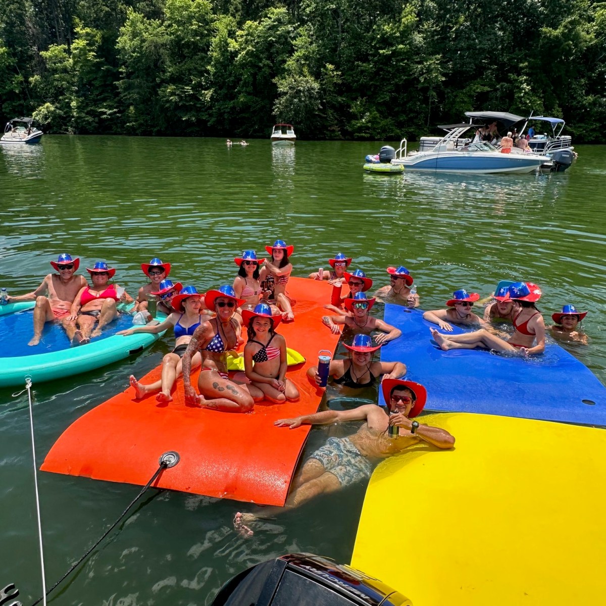 Group wearing patriotic hats on colorful floats in a lake near boats.