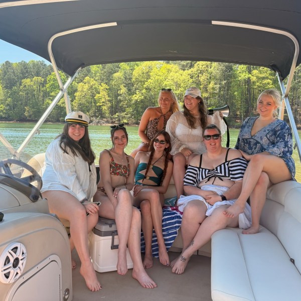 Group of seven people sitting on a boat under a canopy on a sunny day.