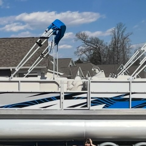 Pontoon boat with blue accents on a trailer in a residential area.