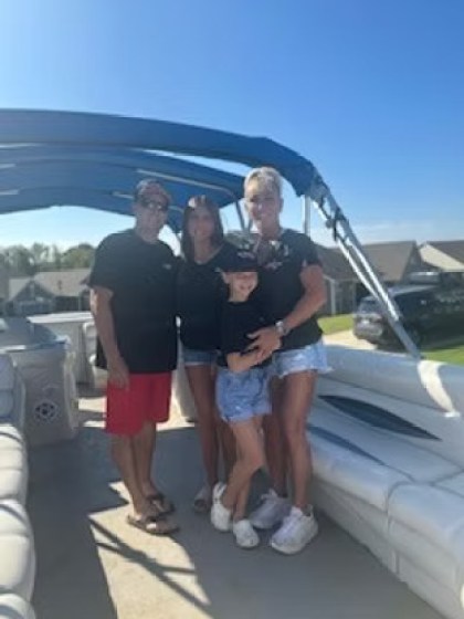 Family of four on a boat, all in black shirts, with a blue canopy and clear sky.