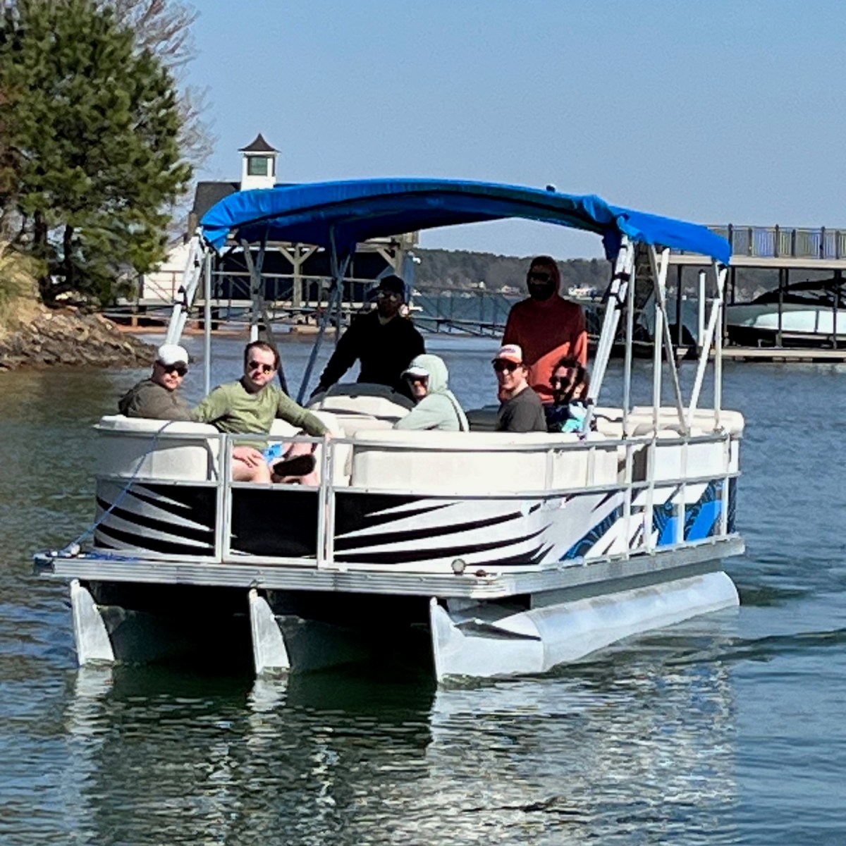 Group of people on a pontoon boat with blue canopy on a sunny day.